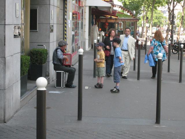The boys are fascinated with the musician playing accordion.